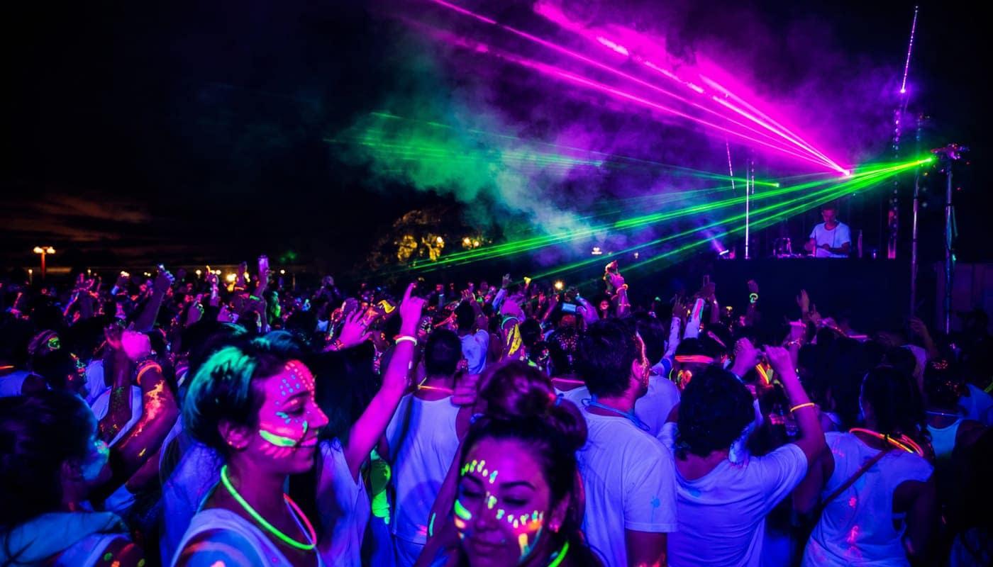 Crowd dancing in fluor body paint under UV lights and lasers at Festichola